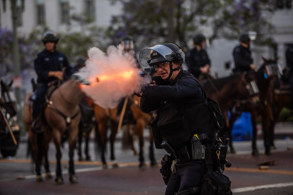 Police officer firing a weapon at protesters during a demonstration in Los Angeles.