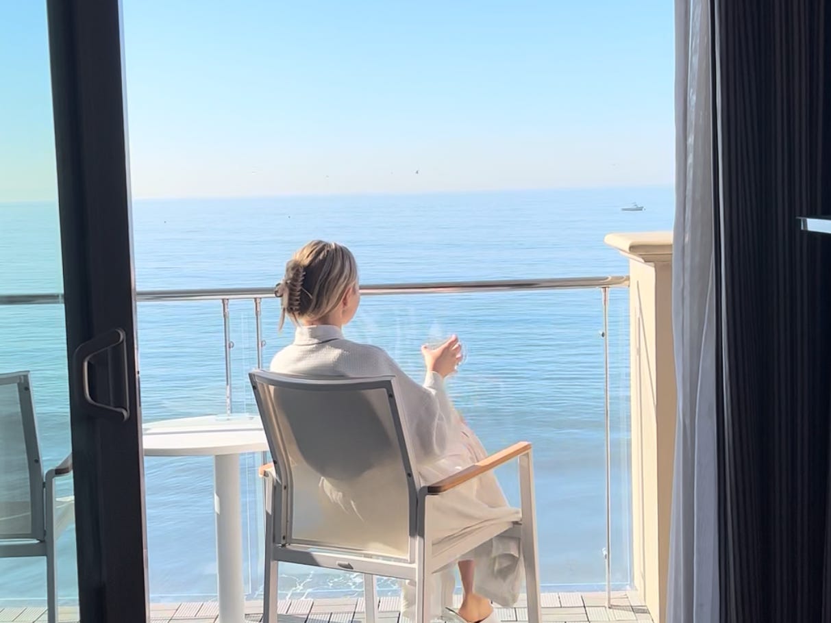 Chloe sits on a balcony holding a wine glass, overlooking the ocean in Malibu.