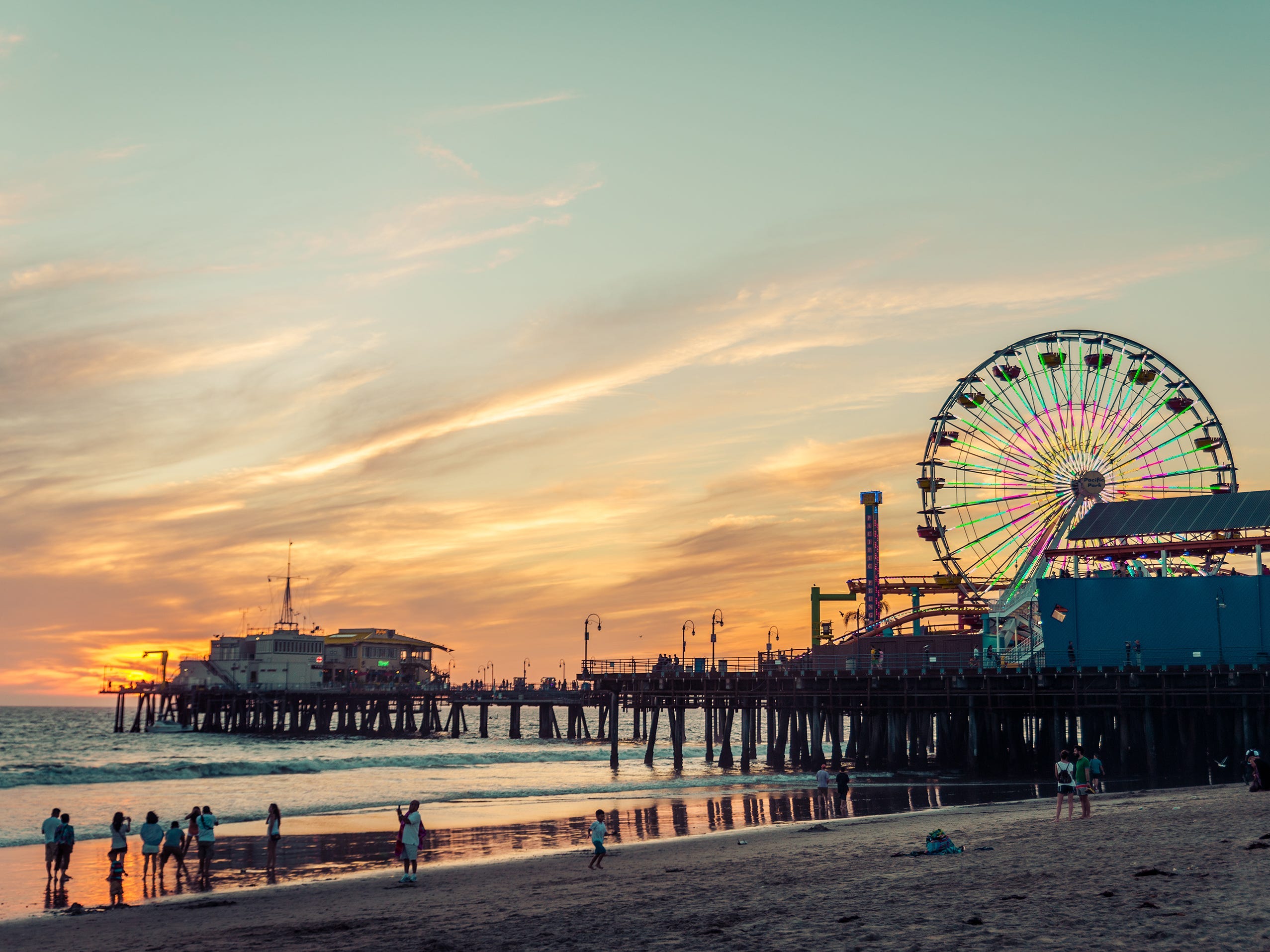 A distant view of a colorful ferris wheel on the Santa Monica Pier at sunset.