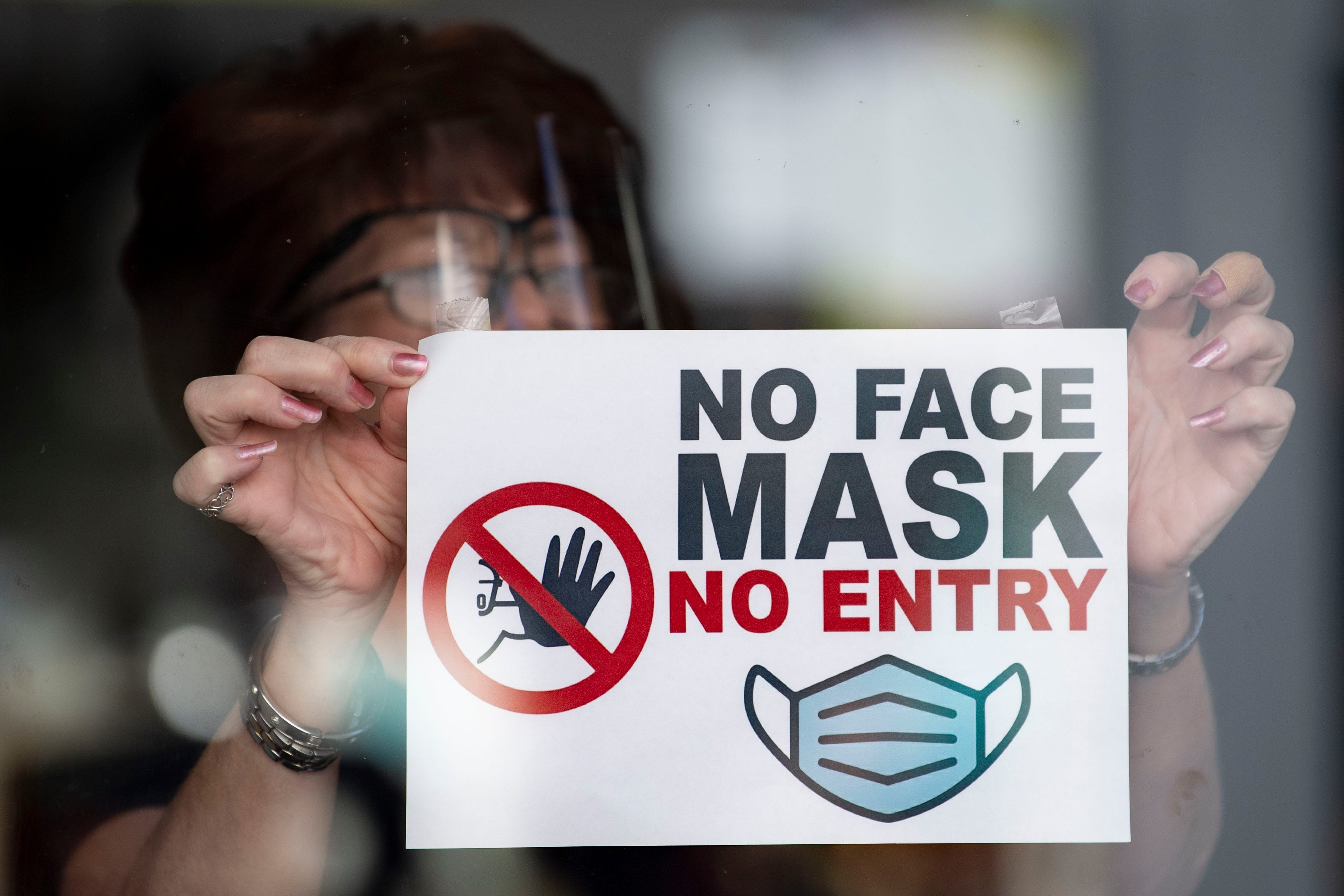 In this photo illustration a woman puts a sign saying "no face mask no entry" in a shop window on September 14, 2020 in Newport, Wales