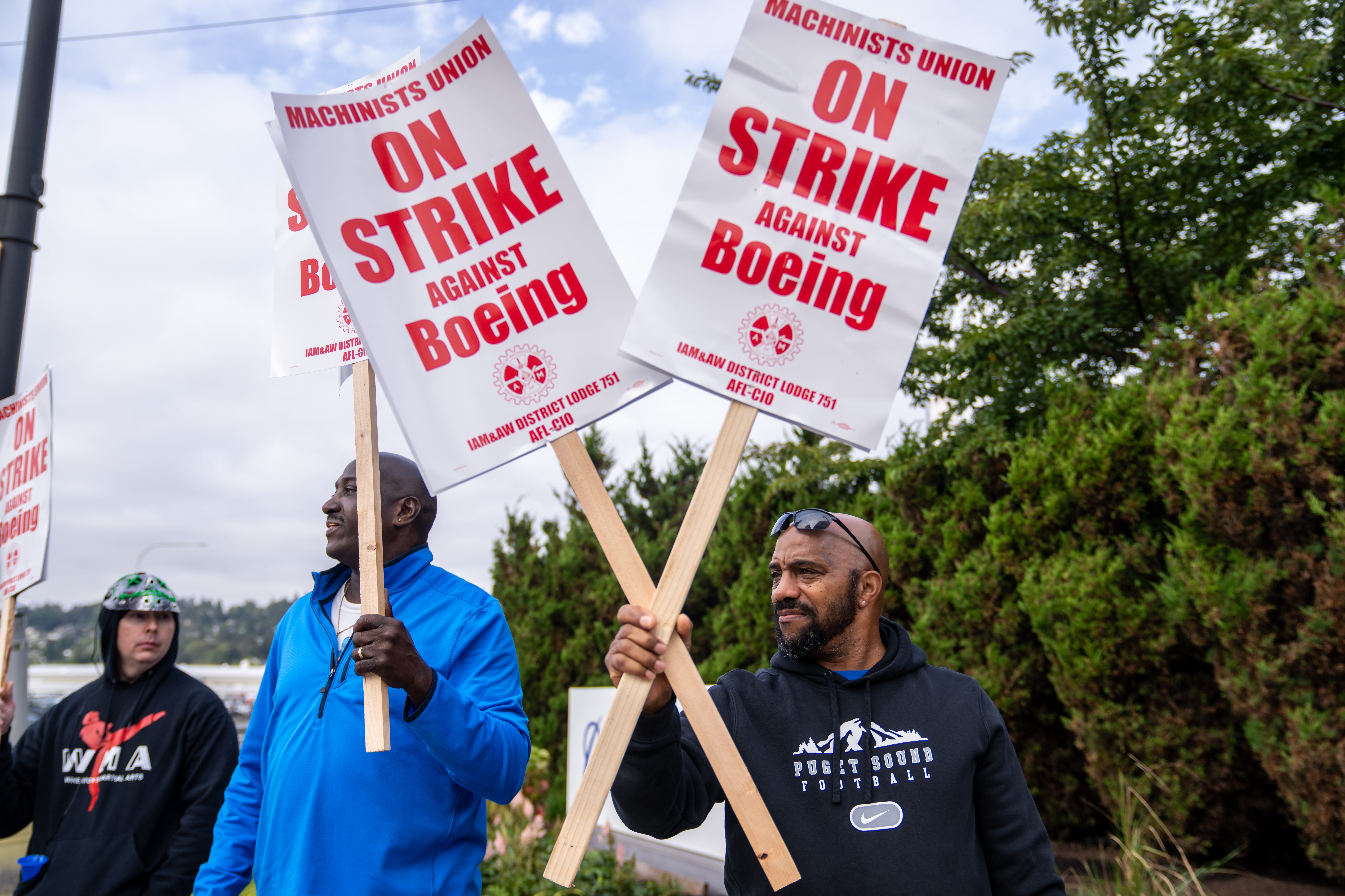 A worker holding up two signs that say "Machinists union on strike against Boeing."