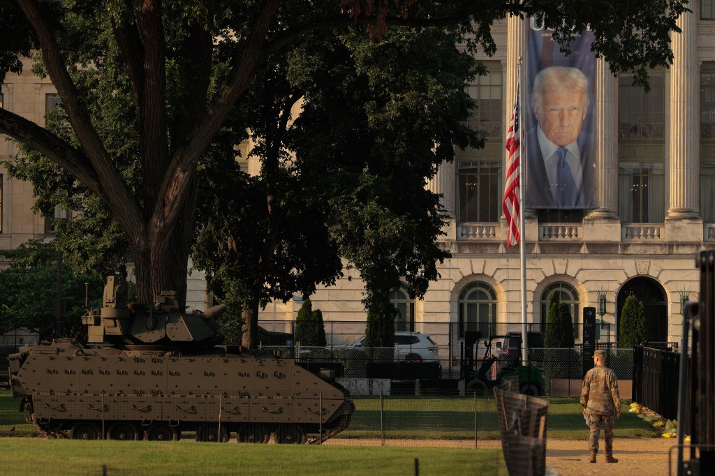 Military vehicle and a large banner of Donald Trump displayed near the Department of Agriculture in Washington, D.C.  A soldier is visible in the background.