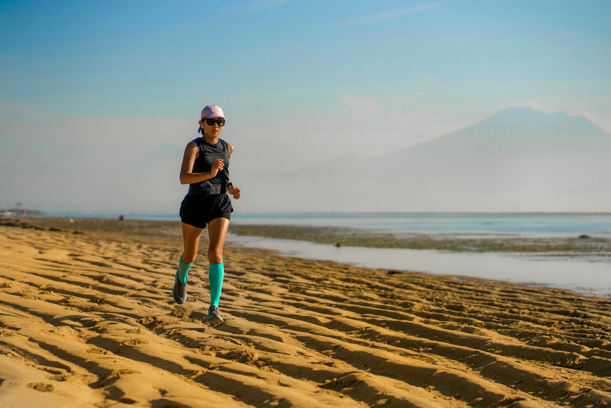 A woman running on a beach in compression socks.