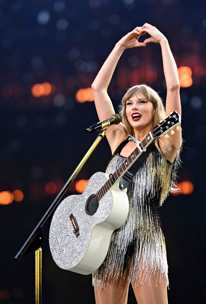 Taylor Swift making a heart with her hands on stage  with a rhinestone guitar.