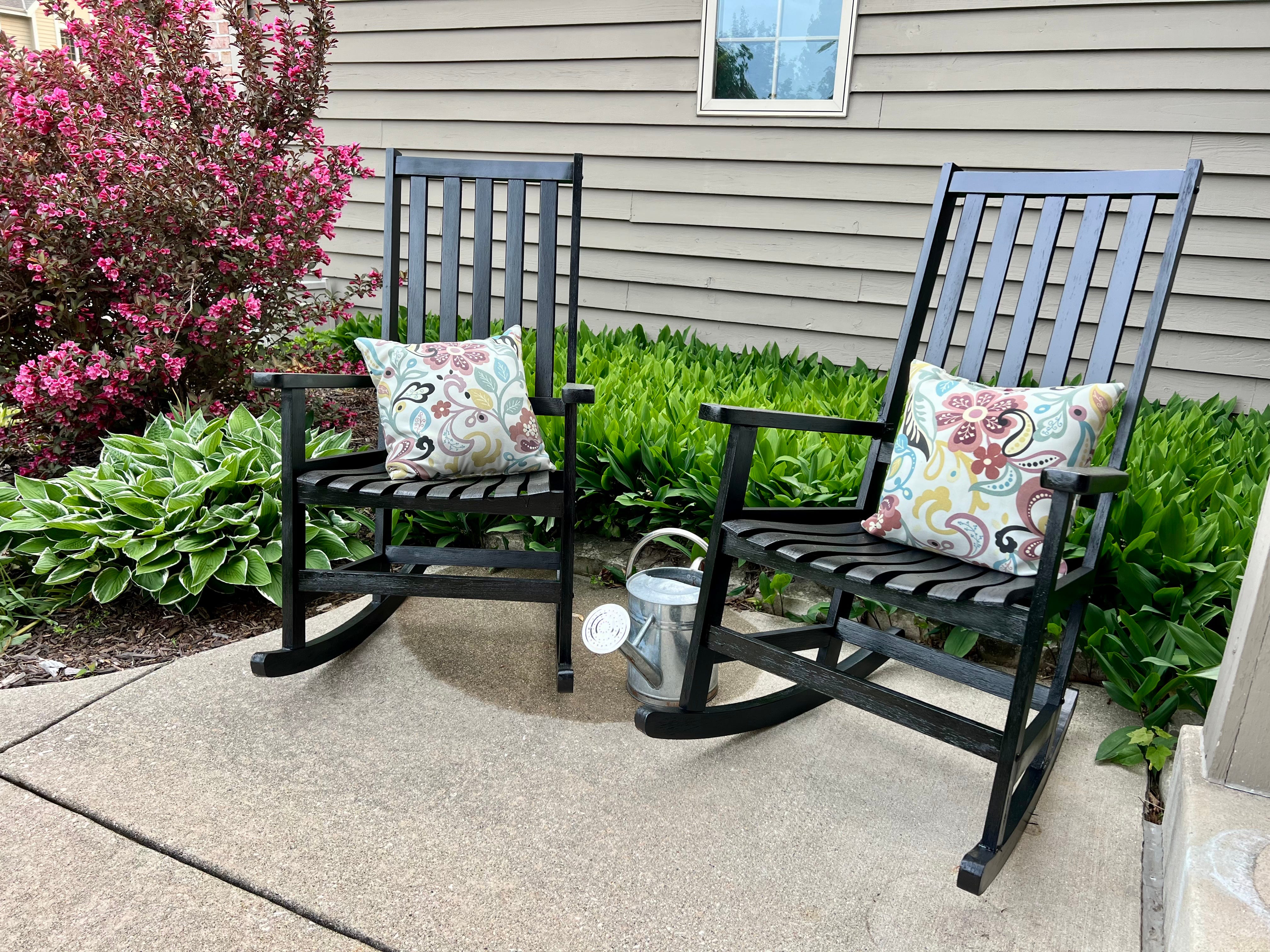Two black rocking chairs sit outside on a paved patio.