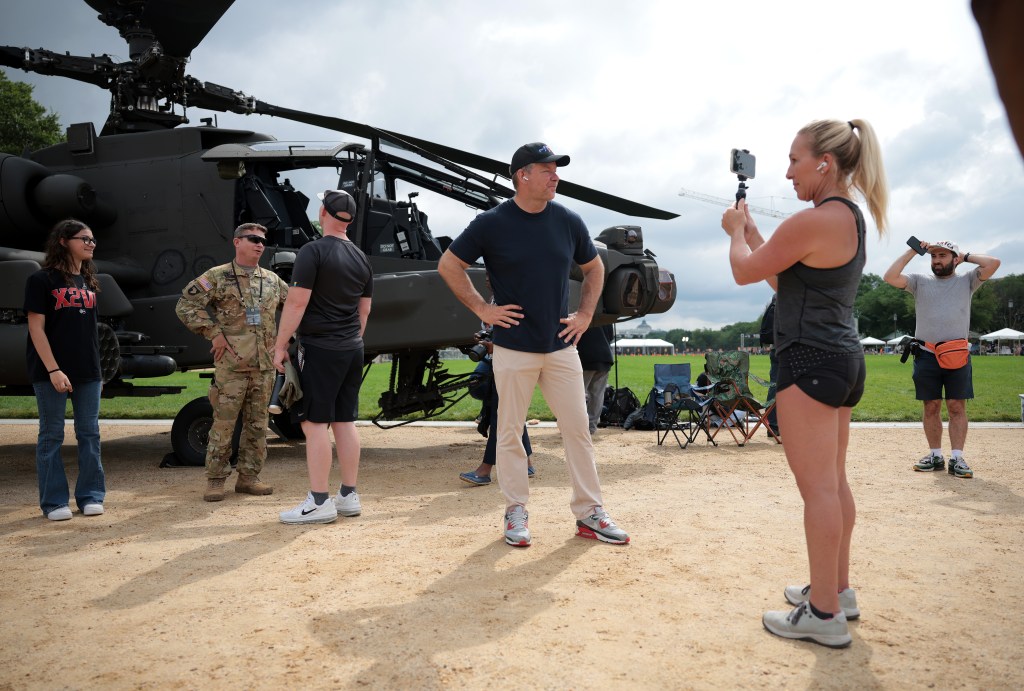 A person filming a man standing near a helicopter at the US Army's 250th Anniversary festival.