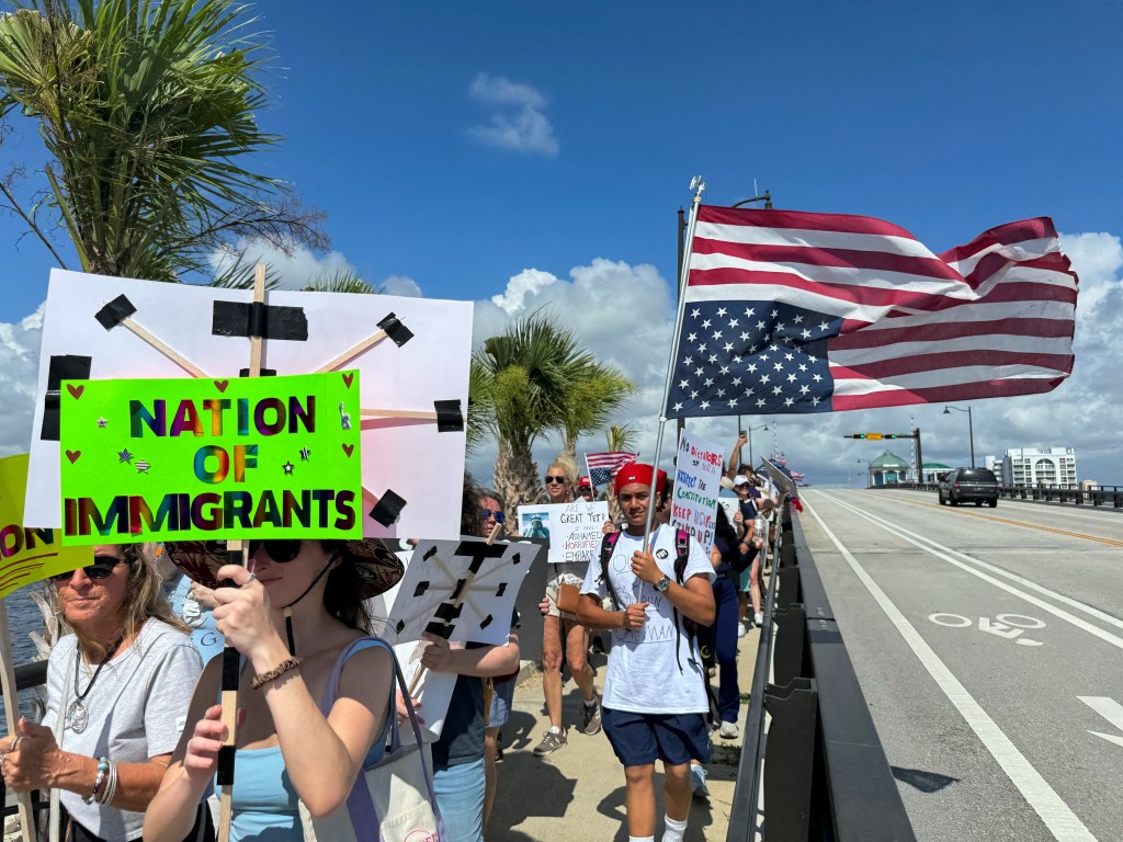 Protestors march, holding signs against President Trump's policies.
