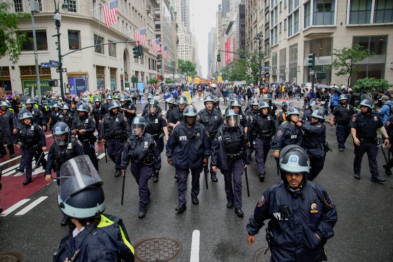 NYPD officers walk along Fifth Avenue in front of demonstrators during the No Kings Day protest.