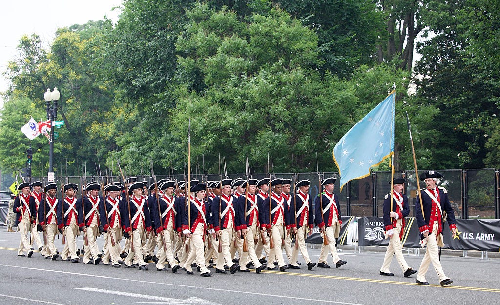 US military service members in Revolutionary War uniform march along Constitution Avenue.