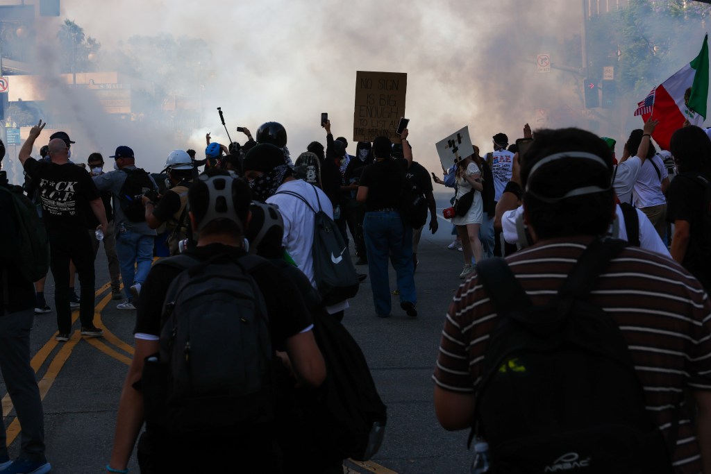 Anti-Trump protesters demonstrating amidst smoke and holding signs.