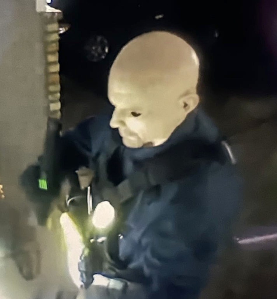 Low-light surveillance image of a person wearing a mask or prosthetic, appearing to be at John Hoffman's home.