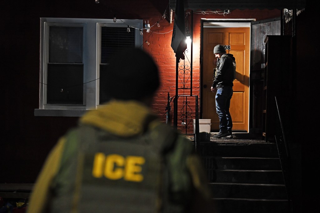 ICE agent at night outside a house.