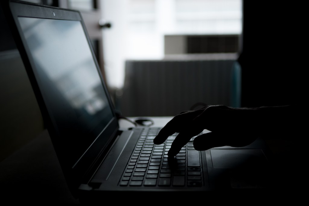 Silhouette of a hand typing on a laptop keyboard in the dark.