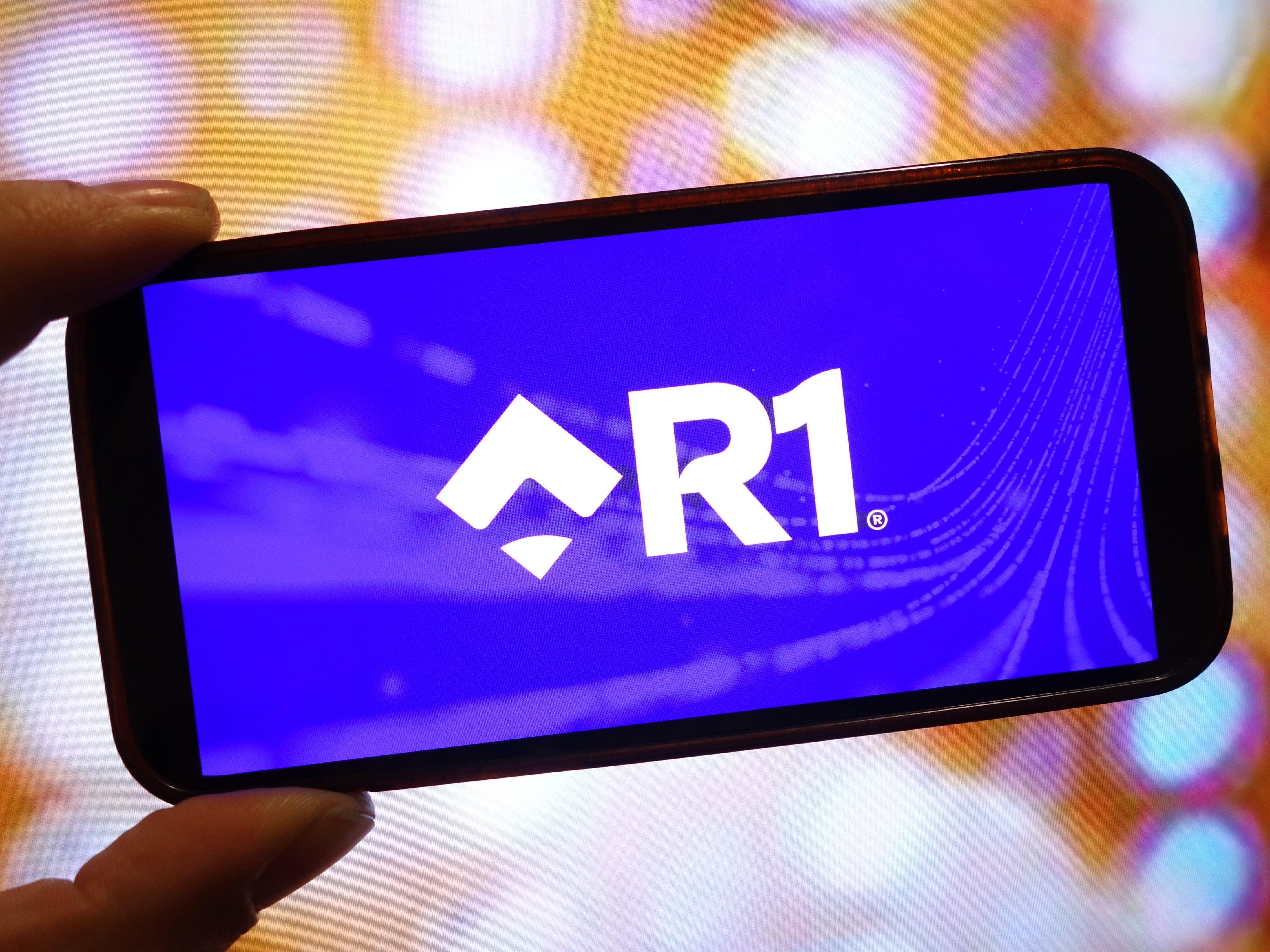 R1 RCM logo on a smartphone screen. R1 RCM was bought by TowerBrook and CD&R last year.