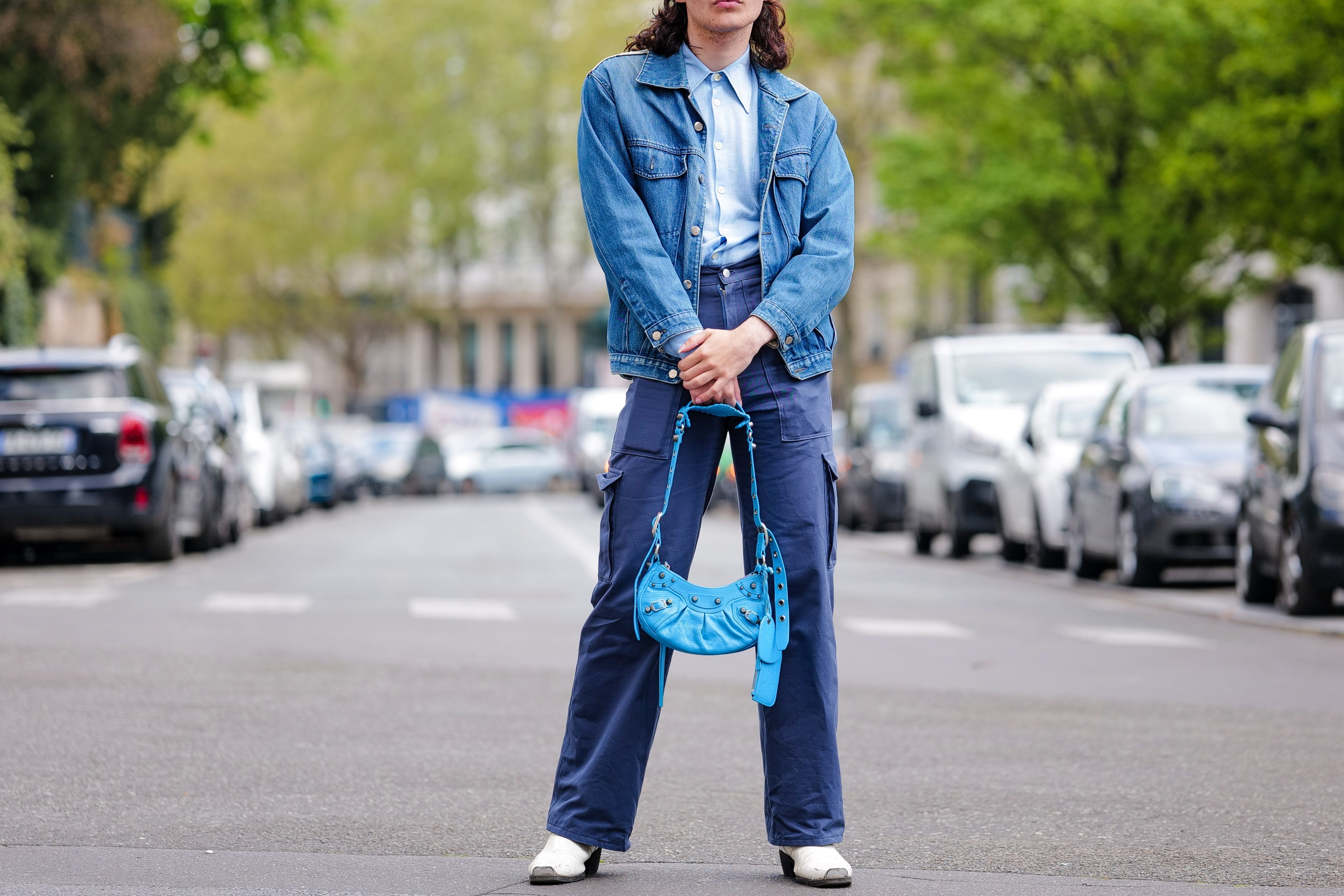 Person wearing denim jacket with dark blue pants holding blue purse