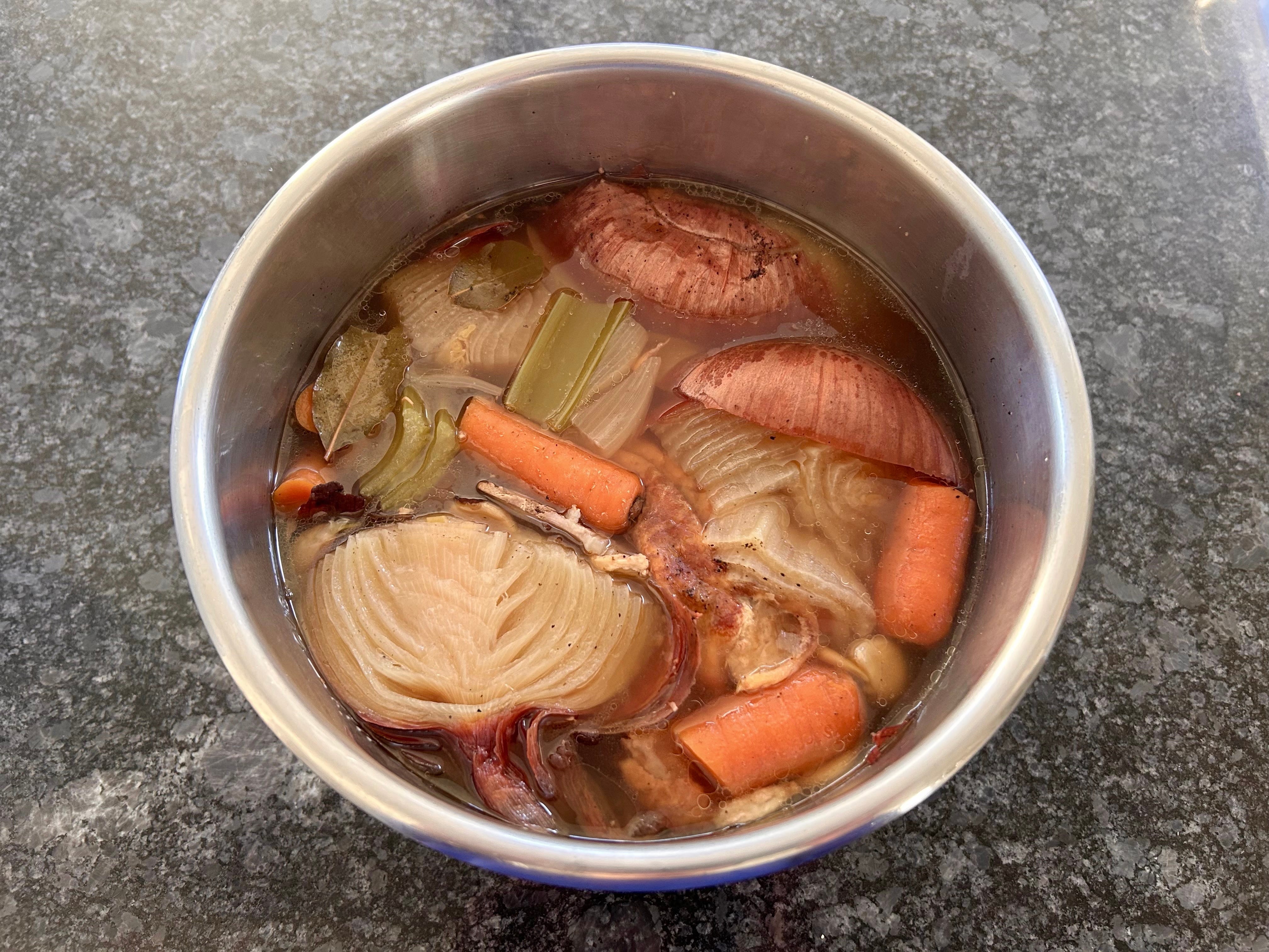 An overhead view of chicken broth and mixed veggies in a crockpot on a kitchen countertop.