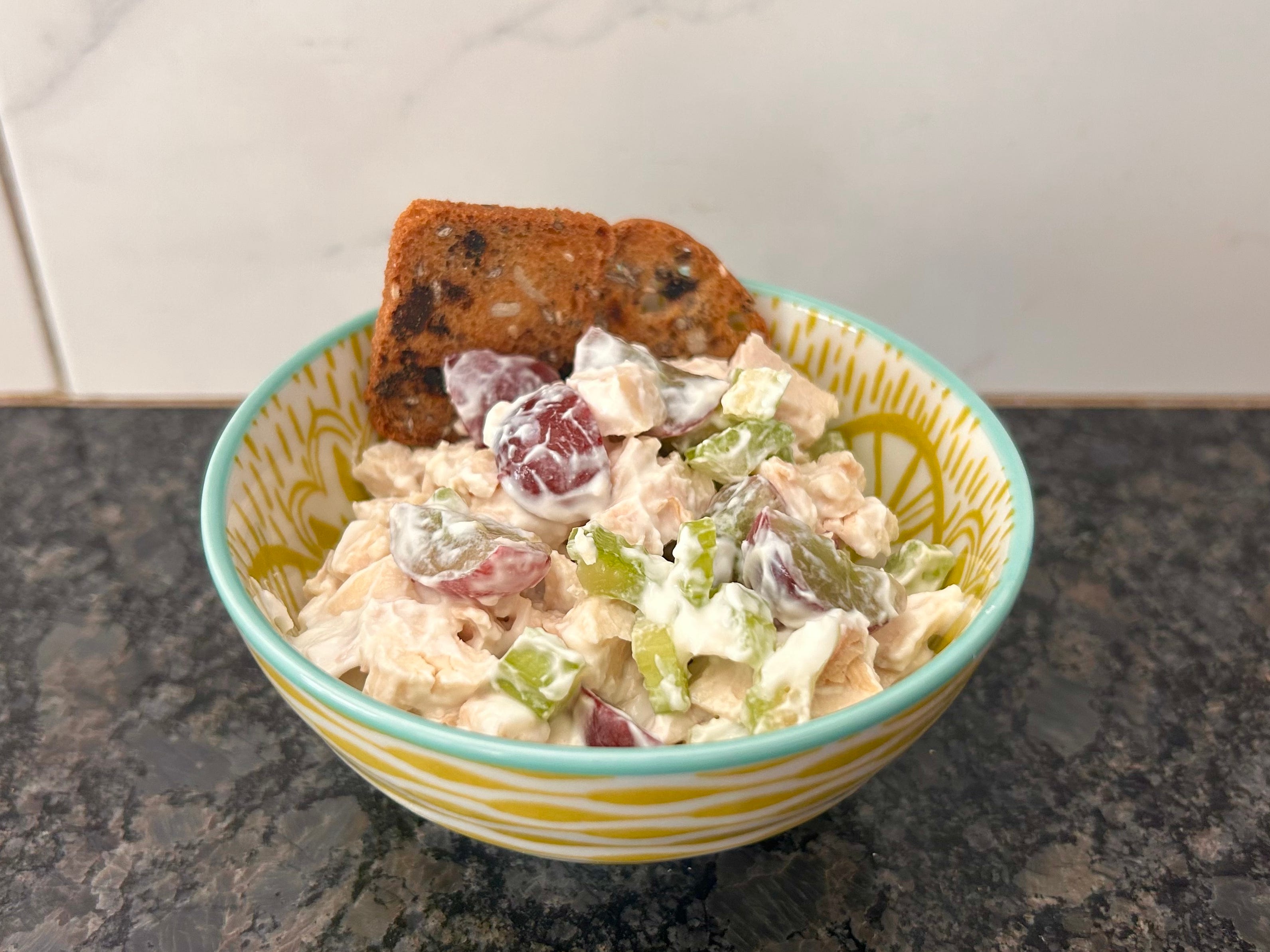 A bowl of Waldorf salad in a colorful bowl on a kitchen countertop.