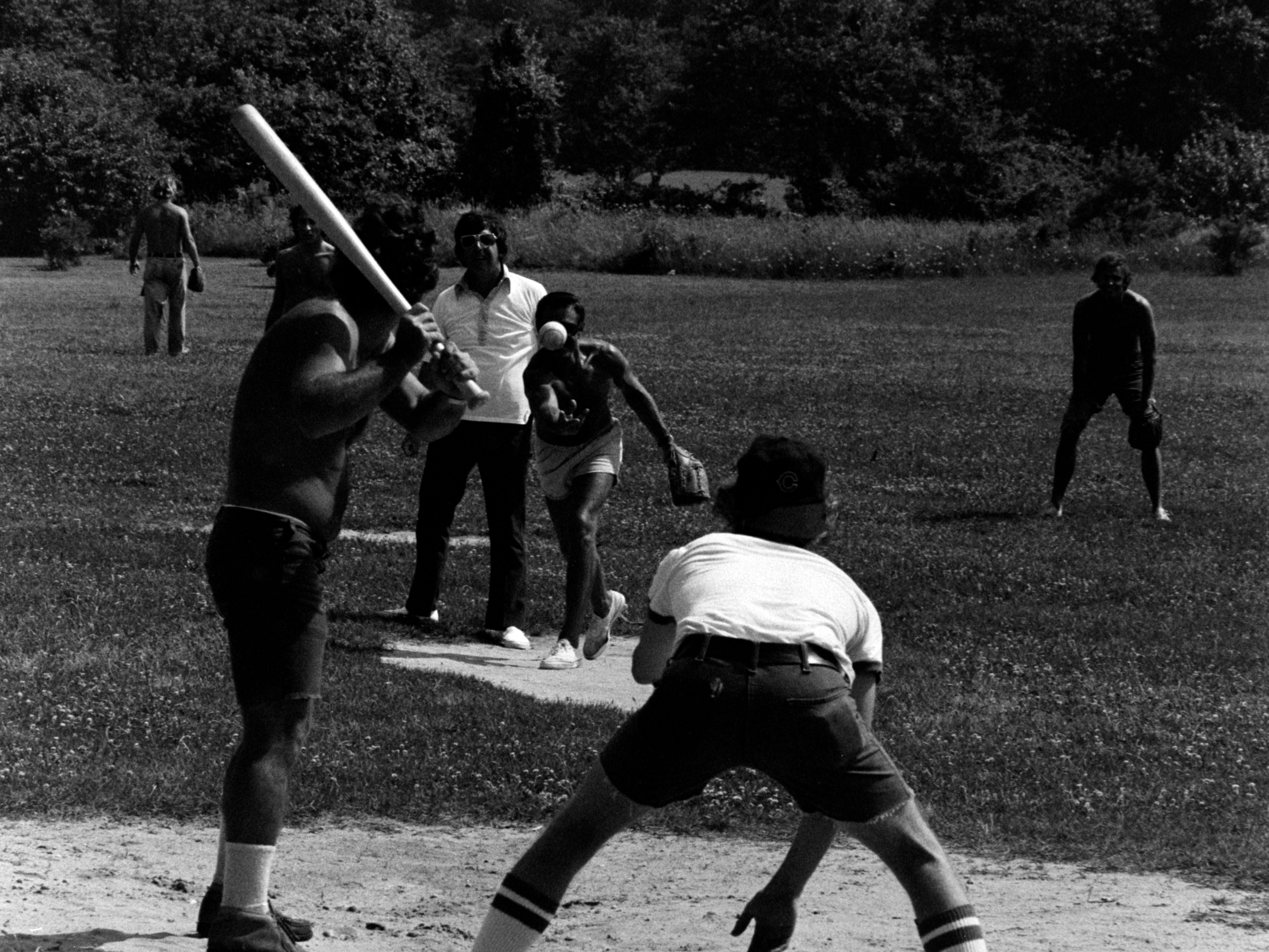 Roy Scheider (C) pitches while playing softball during production of 