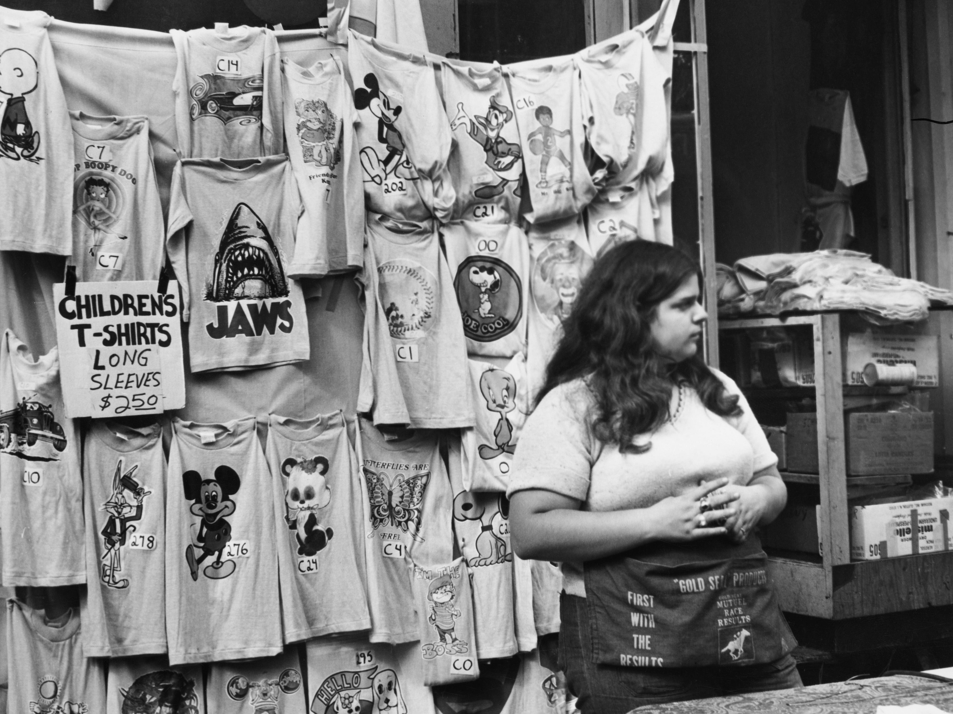 A woman sells printed T-shirts on Bleecker Street in New York City in 1975.