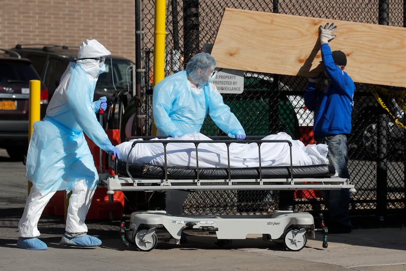 Healthcare workers wheel the body of a deceased person past construction workers