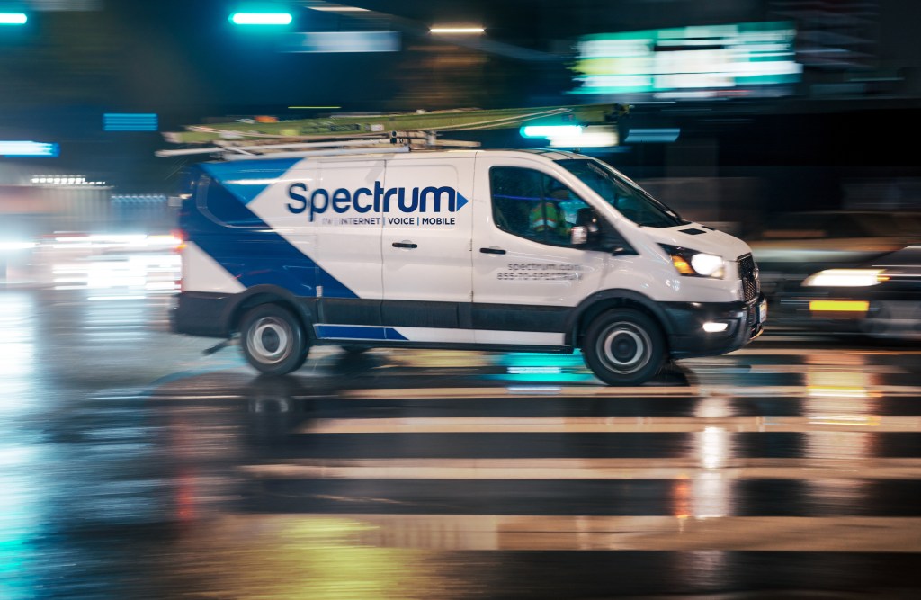 Spectrum service van speeding through city traffic at night in the rain.