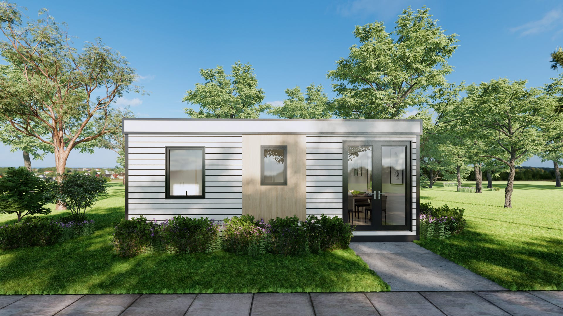 A Hapi tiny home with white panels and windows with black trim sits on a manicured lawn with shrubs and trees around it. The sky is mostly clear and blue. There is a walkway in front of the house.