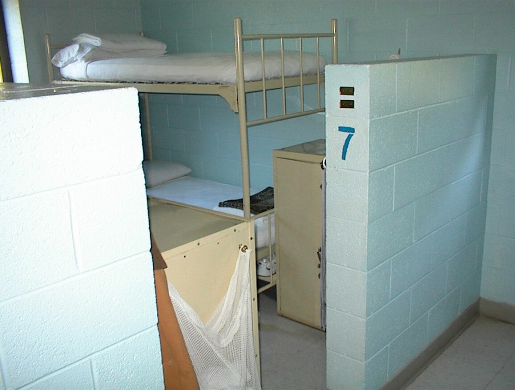 Prison cell with bunk beds and small metal cabinet.
