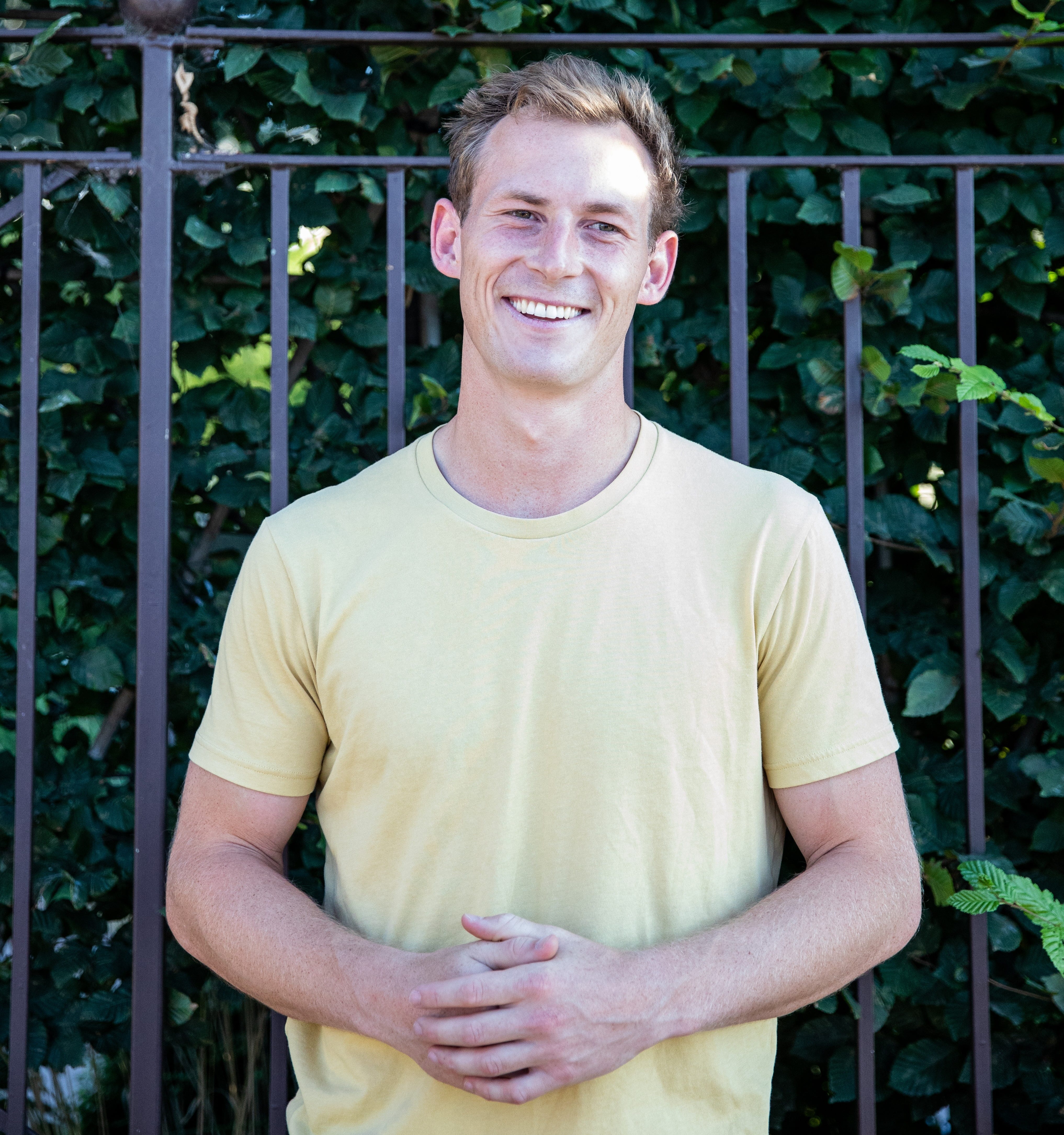 An image of a man in a yellow shirt smiling with his hands in front of him