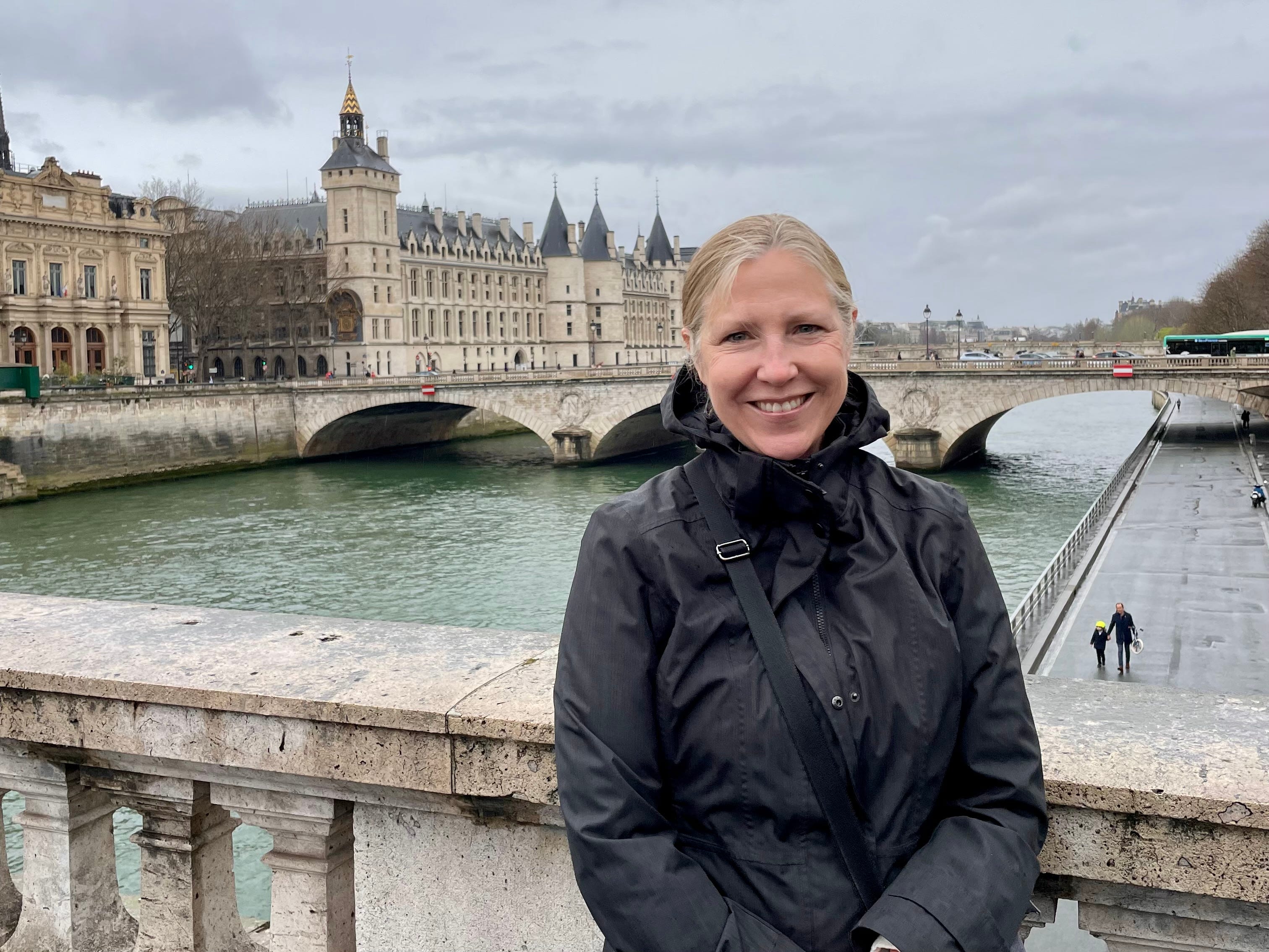 Author Lisa VanderVeen smiling in front of a bridge in cloudy weather