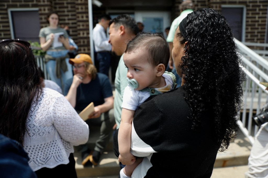 A woman holds her baby while her husband speaks with a lawyer before an ICE appointment.