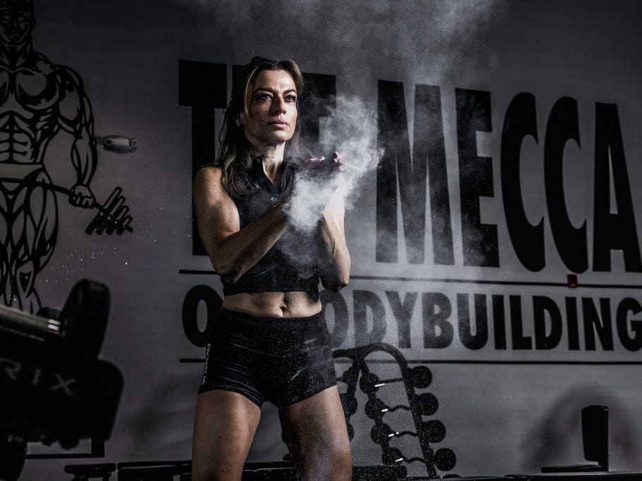 a woman stands in a bodybuilding gym in workout clothes, putting chalk on the hands