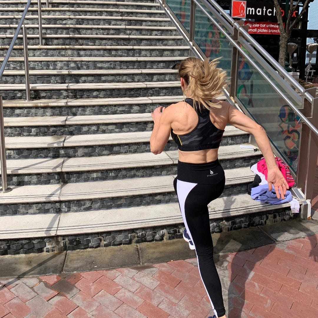 A woman in workout gear running up a flight of stairs.