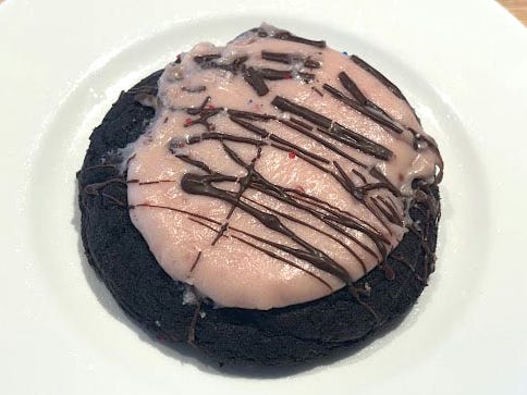 A chocolate cookie topped with pink icing and a chocolate drizzle on a white plate.