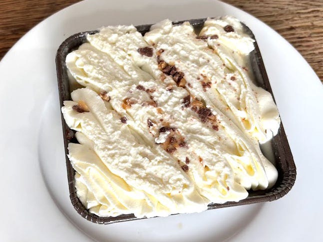 A cake in a small square container with lots of white frosting on top.