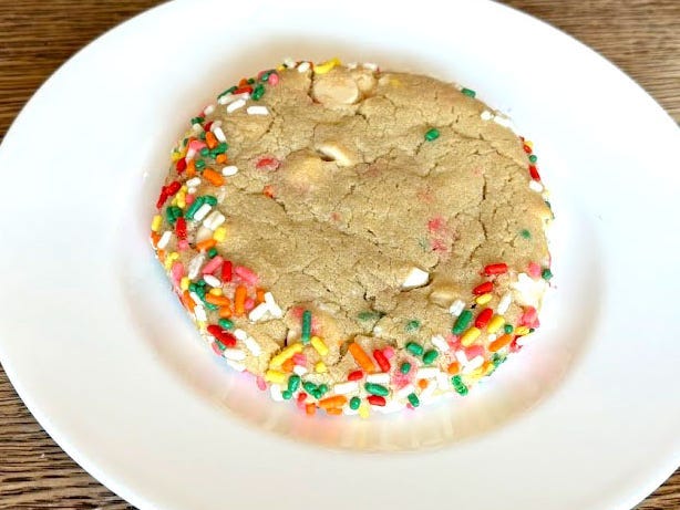 A vanilla cookie with sprinkles on a white plate.