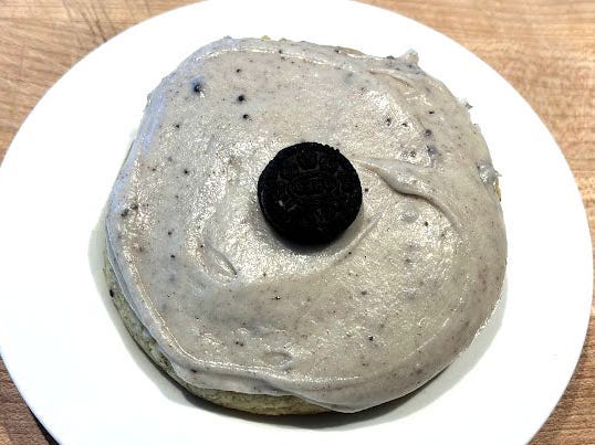 A cookie topped with gray frosting and a mini Oreo on a white plate.