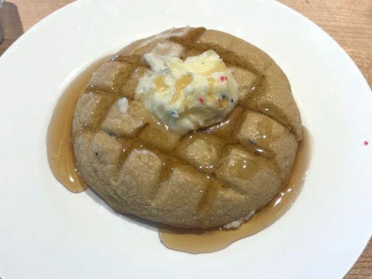 A cookie with lines etched into it, topped with a dollop of icing and syrup, on a white plate.