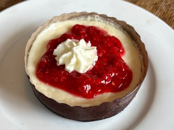 A small cheesecake with raspberry preserves and a small dollop of whipped cream.