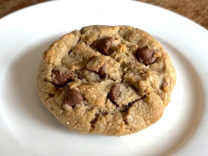 A chocolate-chip Crumbl cookie on a white plate placed on a wooden table.