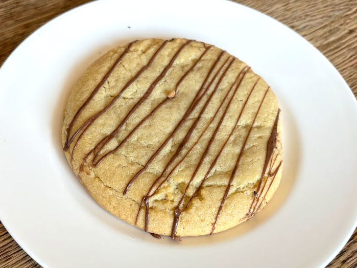 A cookie with a hazelnut drizzle on a white plate.
