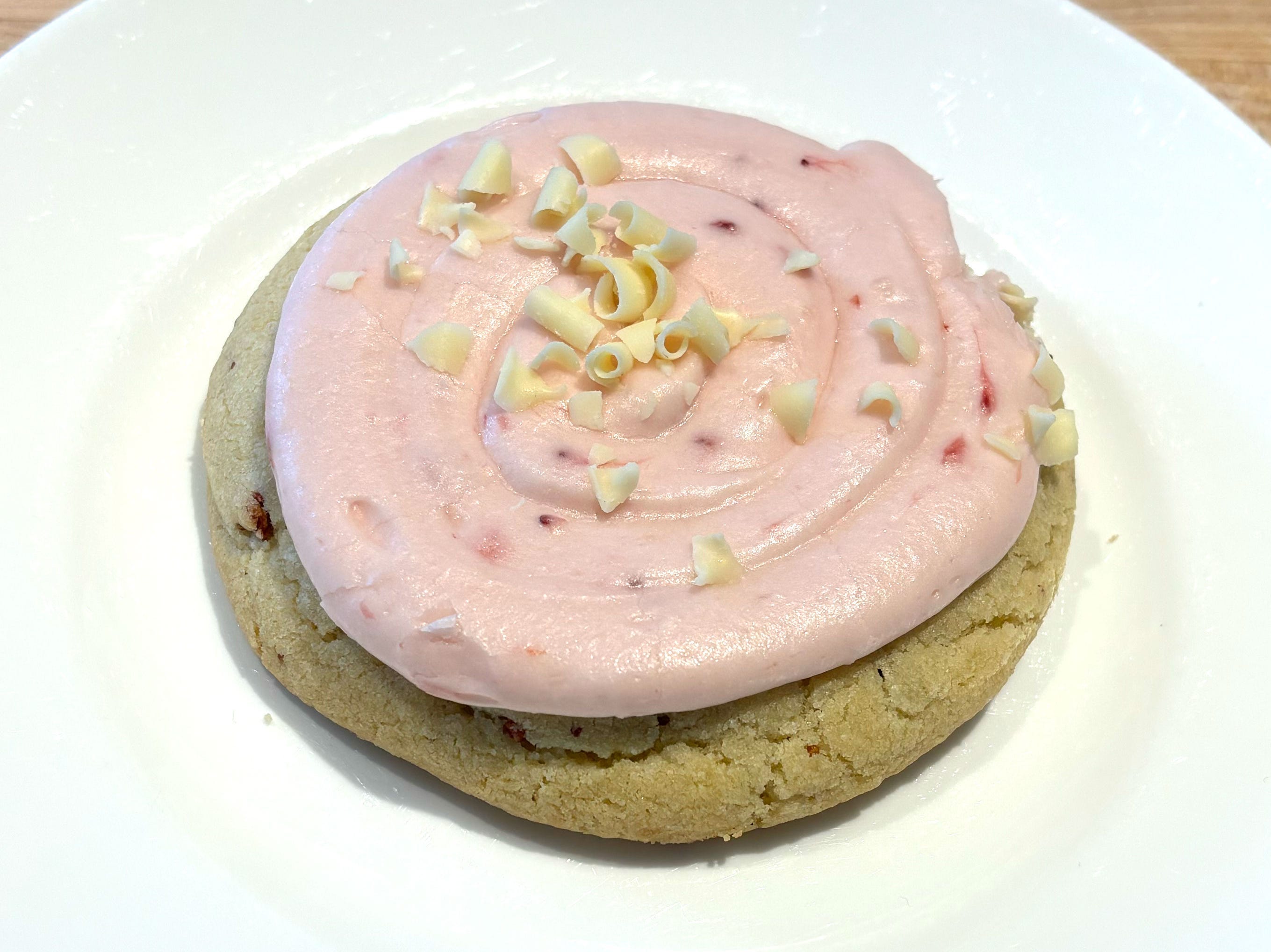 A cookie topped with pink icing and white-chocolate curls on a white plate.