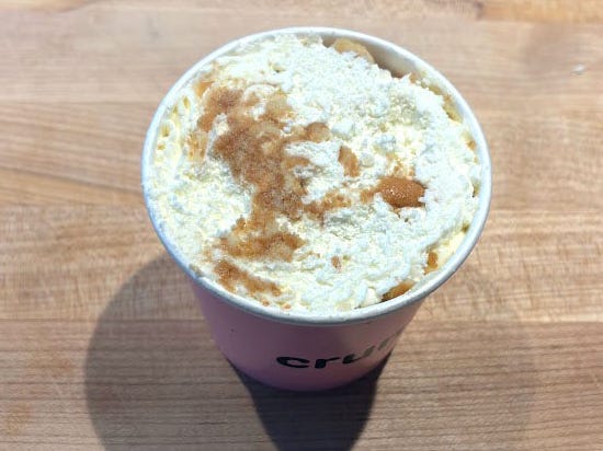 Banana pudding in a paper cup on a wood surface.