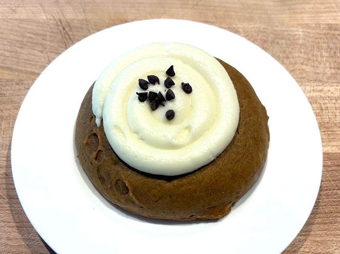 A brown cookie topped with white swirled icing and chocolate chips.