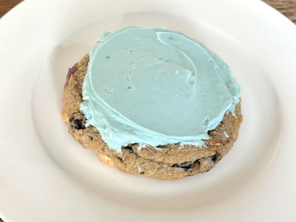 A cookies-and-cream cookie topped with blueish-green frosting on a white plate.