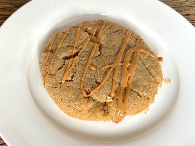A peanut-butter cookie topped with a peanut-butter drizzle on a white plate.