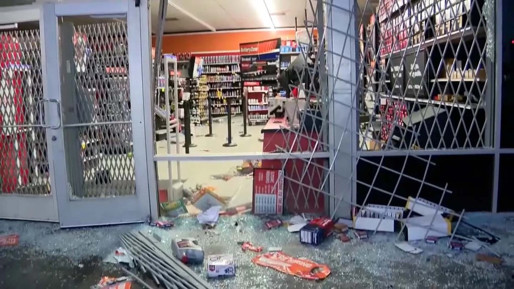 ransacked AutoZone store with broken windows and merchandise strewn on the floor.