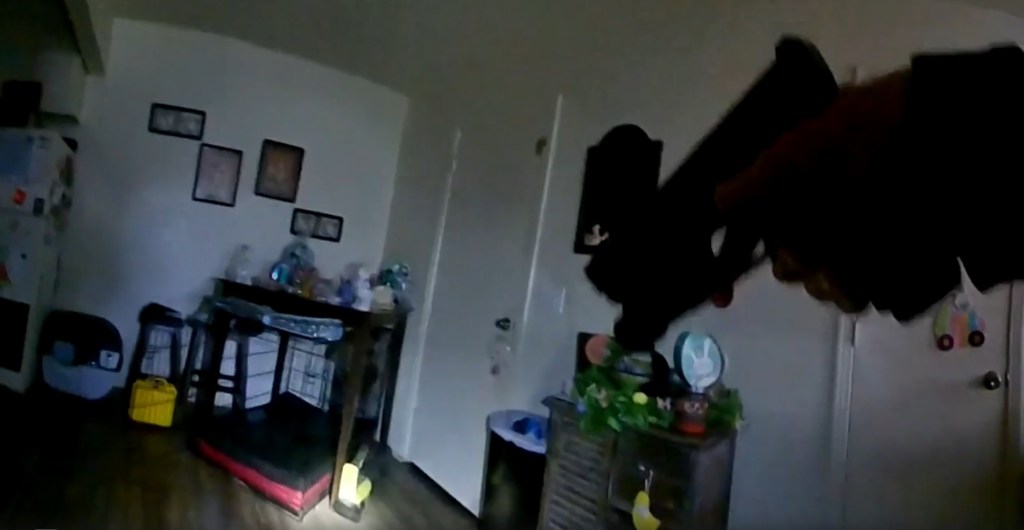 Police bodycam footage of a room with a dog cage and a gun.