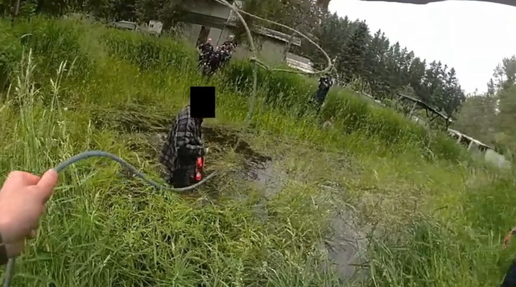 Deputies apprehending a chainsaw-wielding suspect in a swampy area.
