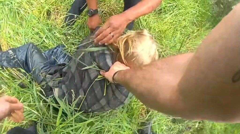 Deputies apprehending a suspect in a grassy field.