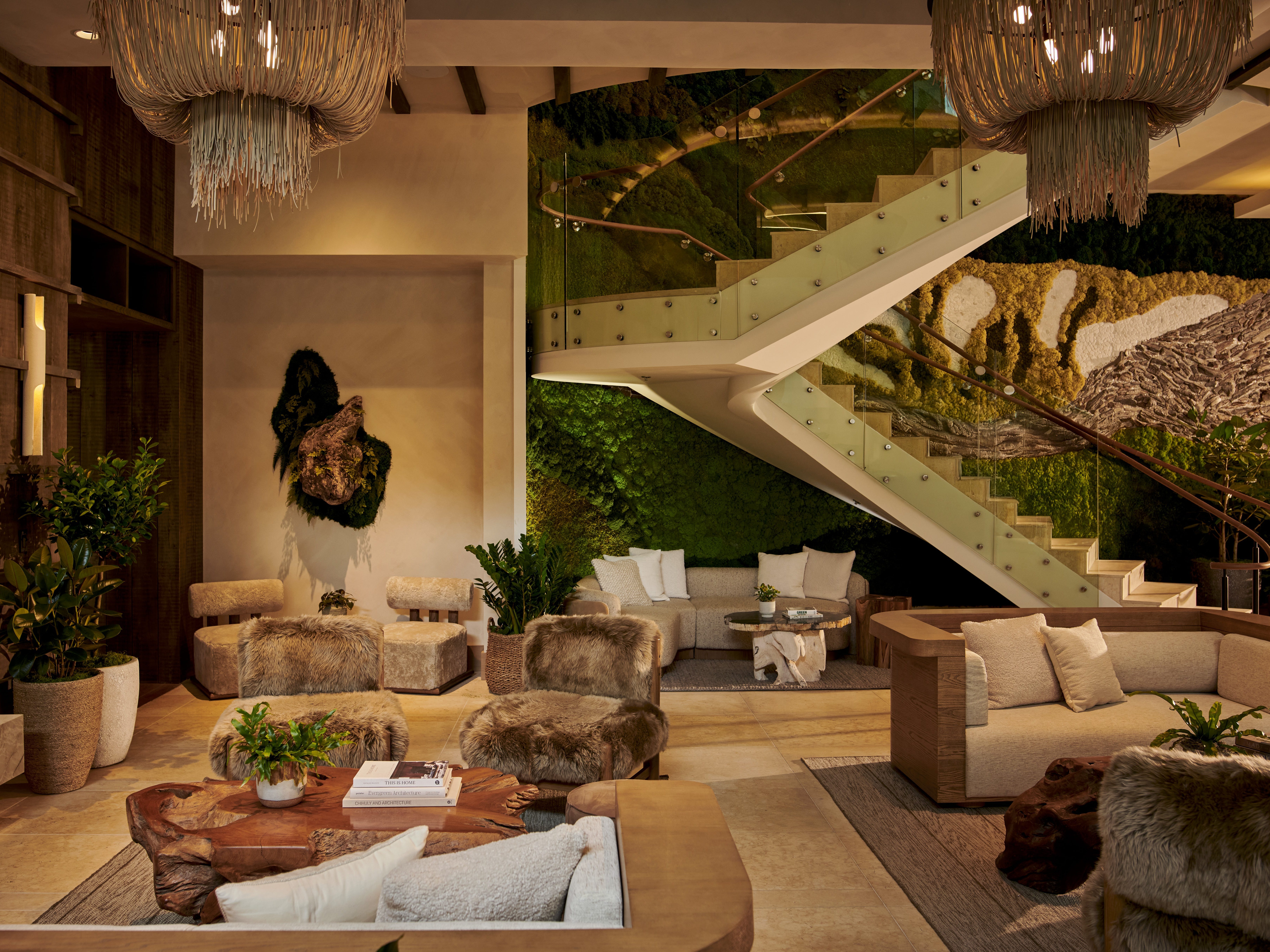 Inside a dimly lit hotel lobby with organic materials, a staircase in front of a living wall, and natural furniture